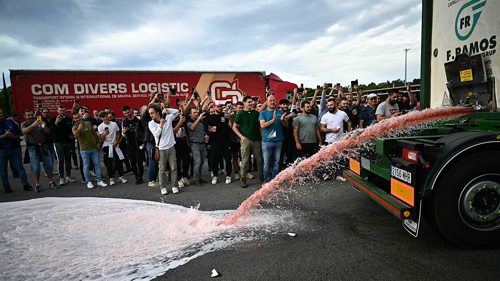 Protesters watch Spanish red wine streaming out of a truck.